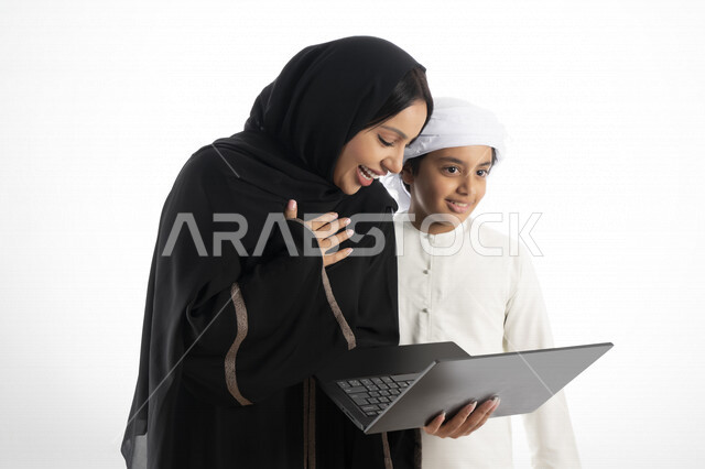 بورتريه لأم عربية خليجية إماراتية ترتدي الزي التقليدي الإماراتي شيلة وعباية ، تعليم الطفل كيفية استخدام الكمبيوتر في المدرسة، استخدام لوحة المفاتيح للكتابة، التعليم الالكتروني، التعليم الفعال، خلفية بيضاء 
