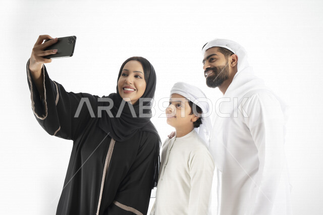 بورتريه لعائلة إمارتية عربية خليجيه  مستمتعتان بالتقاط صورة سيلفي من خلال الهاتف المحمول، التقاط صور تذكارية ، صورة جماعية ، توثيق اللحظات السعيدة، اجراء مكالمة فيديو ، خلفية بيضاء 