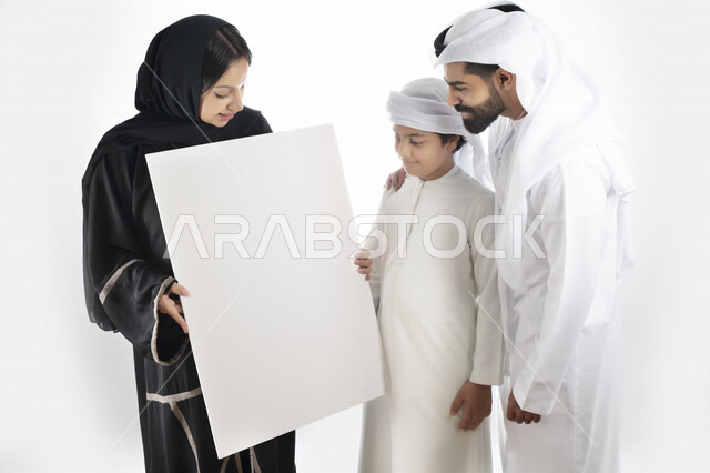 Portrait of an Arab Emirati Gulf family holding an empty white board in their hands, spending fun family time, happy family atmosphere, white background