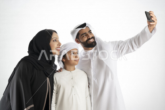 Portrait of an Emirati Arab Gulf family enjoying taking a selfie with a mobile phone, taking memorial photos, a group photo, documenting happy moments, making a video call, white background