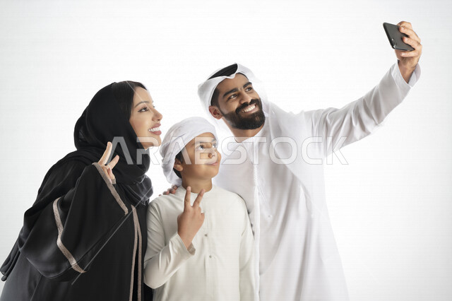 بورتريه لعائلة إمارتية عربية خليجيه  مستمتعتان بالتقاط صورة سيلفي من خلال الهاتف المحمول، التقاط صور تذكارية ، صورة جماعية ، توثيق اللحظات السعيدة، اجراء مكالمة فيديو ، خلفية بيضاء 