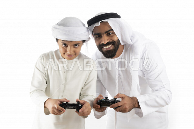 بورتريه لأب وإبن إماراتي خليجي عربي بزي التقلدي ,  يمسكان عصا التحكم و يلعبان بألعاب الفيديو، إيماءات وجه تدل على الإندماج والتفاعل مع اللعبه، المتعة و التسلية بألعاب الفيديو، ألعاب البلايستيشن الترفيهية، اللعب مع العائلة , خلفية بيضاء 
