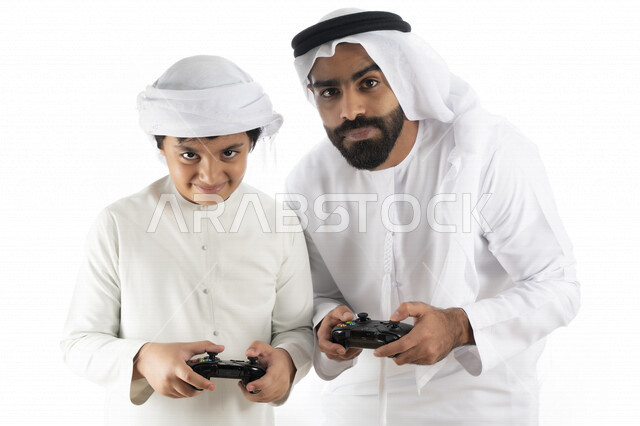 بورتريه لأب وإبن إماراتي خليجي عربي بزي التقلدي ,  يمسكان عصا التحكم و يلعبان بألعاب الفيديو، إيماءات وجه تدل على الإندماج والتفاعل مع اللعبه، المتعة و التسلية بألعاب الفيديو، ألعاب البلايستيشن الترفيهية، اللعب مع العائلة , خلفية بيضاء 