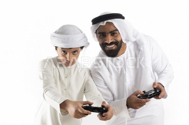 بورتريه لأب وإبن إماراتي خليجي عربي بزي التقلدي ,  يمسكان عصا التحكم و يلعبان بألعاب الفيديو، إيماءات وجه تدل على الإندماج والتفاعل مع اللعبه، المتعة و التسلية بألعاب الفيديو، ألعاب البلايستيشن الترفيهية، اللعب مع العائلة , خلفية بيضاء 