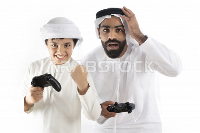 بورتريه لأب وإبن إماراتي خليجي عربي بزي التقلدي ,  يمسكان عصا التحكم و يلعبان بألعاب الفيديو، إيماءات وجه تدل على الإندماج والتفاعل مع اللعبه، المتعة و التسلية بألعاب الفيديو، ألعاب البلايستيشن الترفيهية، اللعب مع العائلة , خلفية بيضاء 