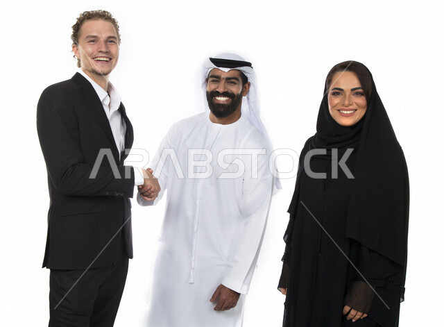 الإتفاق والتعاون بين الشركات على الأعمال والمشاريع التجارية، بورتريه لفريق عمل عربي خليجي اماراتي في اجتماع عمل مع عميل أجنبي جديد يرتدي البدلة الرسمية، رجلان اعمال يتصافحان لاتمام صفقة عمل ناجحة، تحقيق استراتيجيات وأهداف العمل، خلفية بيضاء
