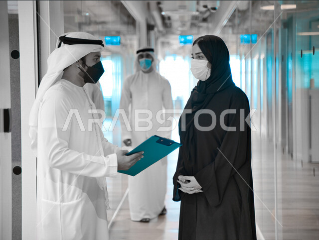 رجل وإمرأه عربيان إماراتيان خليجيان يرتديان الكمامة في مقر الشركه، العوده بحذر، اتباع اجراءات الوقاية والسلامة من فايروس كورونا, حوارات ونقاشات عمل, زملاء عمل, شركات عربيه إماراتيه خليجيه