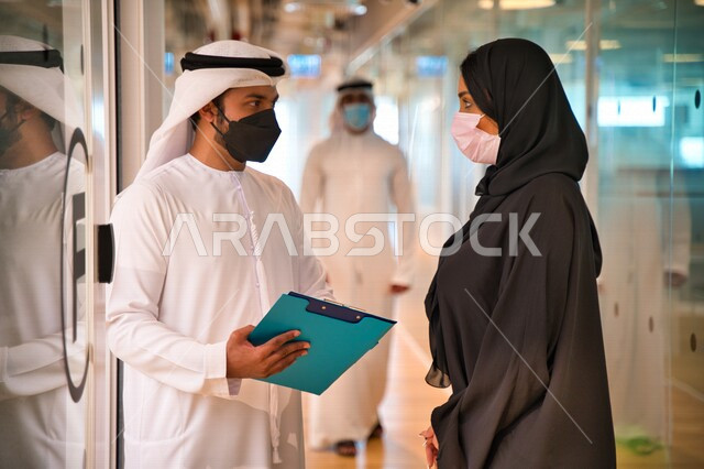 رجل وإمرأه عربيان إماراتيان خليجيان يرتديان الكمامة في مقر الشركه، العوده بحذر، اتباع اجراءات الوقاية والسلامة من فايروس كورونا, حوارات ونقاشات عمل, زملاء عمل, شركات عربيه إماراتيه خليجيه