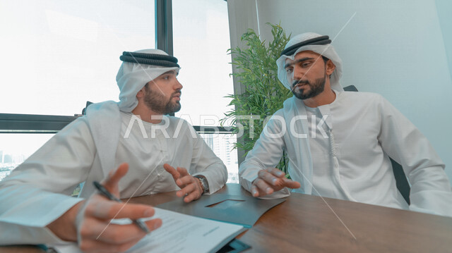 رجال اعمال عرب خليجيين اماراتيين يتناقشون في عقد العمل في مقر الشركة، شركاء عمل، اجتماع عمل، عقد عمل جديد، عقد شراكة، قراءة البنود الخاصة بالعقد، التحقق والتدقيق في شروط العقد، الموافقة على الشروط، التوقيع على العقود