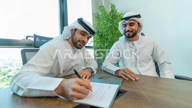 رجال اعمال عرب خليجيين اماراتيين يتناقشون في عقد العمل في مقر الشركة، شركاء عمل، اجتماع عمل، عقد عمل جديد، عقد شراكة، قراءة البنود الخاصة بالعقد، التحقق والتدقيق في شروط العقد، الموافقة على الشروط، التوقيع على العقود