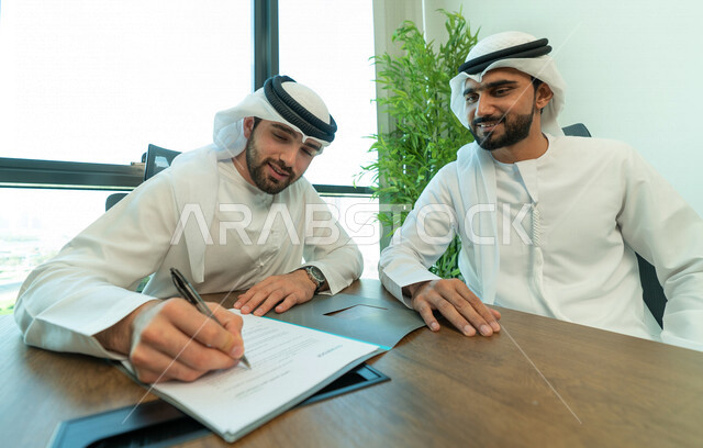 رجال اعمال عرب خليجيين اماراتيين يتناقشون في عقد العمل في مقر الشركة، شركاء عمل، اجتماع عمل، عقد عمل جديد، عقد شراكة، قراءة البنود الخاصة بالعقد، التحقق والتدقيق في شروط العقد، الموافقة على الشروط، التوقيع على العقود