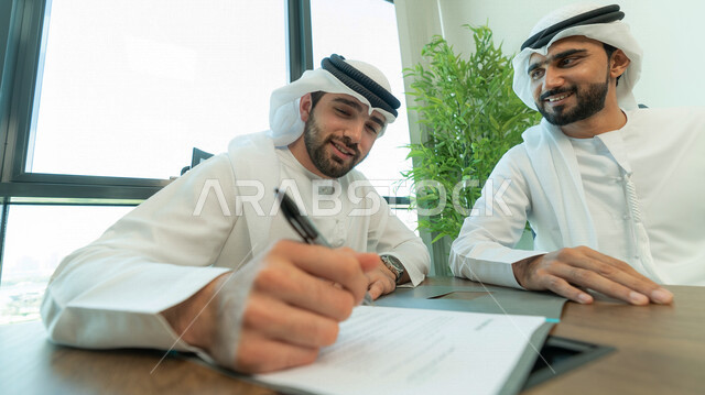 رجال اعمال عرب خليجيين اماراتيين يتناقشون في عقد العمل في مقر الشركة، شركاء عمل، اجتماع عمل، عقد عمل جديد، عقد شراكة، قراءة البنود الخاصة بالعقد، التحقق والتدقيق في شروط العقد، الموافقة على الشروط، التوقيع على العقود