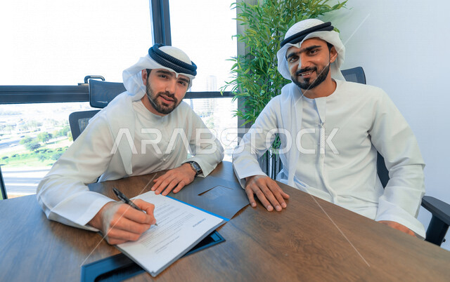 رجال اعمال عرب خليجيين اماراتيين يتناقشون في عقد العمل في مقر الشركة، شركاء عمل، اجتماع عمل، عقد عمل جديد، عقد شراكة، قراءة البنود الخاصة بالعقد، التحقق والتدقيق في شروط العقد، الموافقة على الشروط، التوقيع على العقود