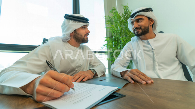 رجال اعمال عرب خليجيين اماراتيين يتناقشون في عقد العمل في مقر الشركة، شركاء عمل، اجتماع عمل، عقد عمل جديد، عقد شراكة، قراءة البنود الخاصة بالعقد، التحقق والتدقيق في شروط العقد، الموافقة على الشروط، التوقيع على العقود