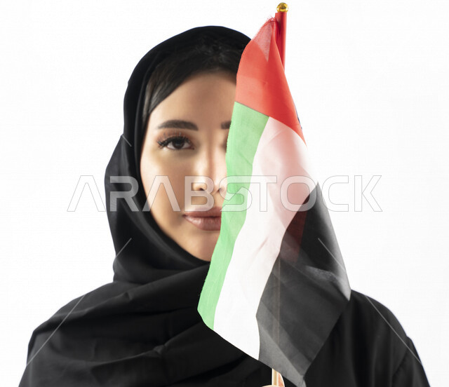 بورتريه لمرأة عربية خليجية إماراتية، مبتسمة تنظر إلى الكاميرا، تحمل علم الإمارات العربية المتحدة، الإحتفال باليوم الوطني الإماراتي، هوية اليوم الوطني الإماراتي 51 ، يوم استقلال الإمارات، حب الوطن، العيد الوطني الإماراتي