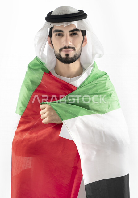 بورتريه لرجل عربي خليجي إماراتي، ينظر إلى الكاميرا، بالزي الإماراتي التقليدي، يحمل علم الإمارات العربية المتحدة على ظهره، الإحتفال باليوم الوطني الإماراتي، هوية اليوم الوطني الإماراتي 51 ، يوم استقلال الإمارات، حب الوطن، العيد الوطني الإماراتي
