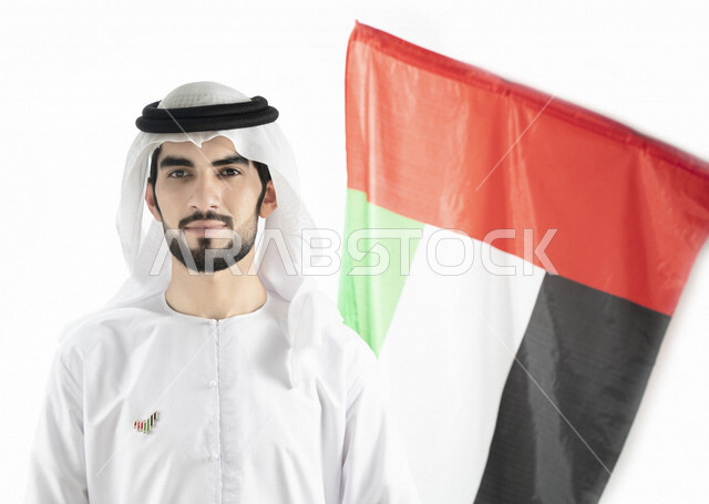 بورتريه لرجل عربي خليجي إماراتي، ينظر إلى الكاميرا، بالزي الإماراتي التقليدي، خلفية لعلم الإمارات العربية المتحدة، تعليق شعار اليوم الوطني على صدره، الإحتفال باليوم الوطني الإماراتي، هوية اليوم الوطني الإماراتي 51 ، يوم استقلال الإمارات، حب الوطن