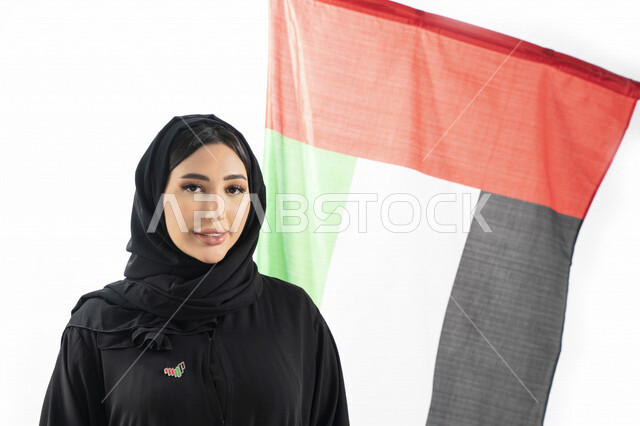 بورتريه لمرأة عربية خليجية إماراتية، مبتسمة تنظر إلى الكاميرا، خلفية لعلم الإمارات العربية المتحدة، تعليق شعار اليوم الوطني على صدرها، الإحتفال باليوم الوطني الإماراتي، هوية اليوم الوطني الإماراتي 51 ، يوم استقلال الإمارات، العيد الوطني الإماراتي