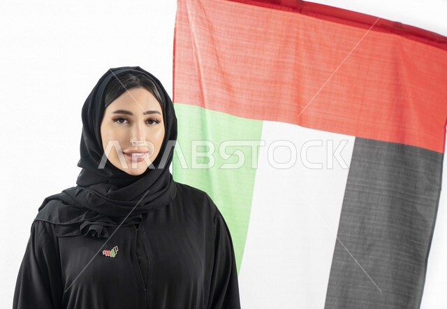بورتريه لمرأة عربية خليجية إماراتية، مبتسمة تنظر إلى الكاميرا، خلفية لعلم الإمارات العربية المتحدة، تعليق شعار اليوم الوطني على صدرها، الإحتفال باليوم الوطني الإماراتي، هوية اليوم الوطني الإماراتي 51 ، يوم استقلال الإمارات، العيد الوطني الإماراتي