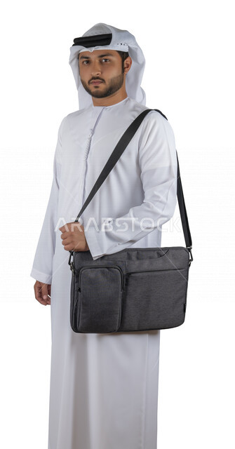 Portrait of an Arab Gulf Emirati university student with a bag on his back, holding a university book in his hand, reading university books, reviewing daily lessons, university education in the United Arab Emirates, white background.