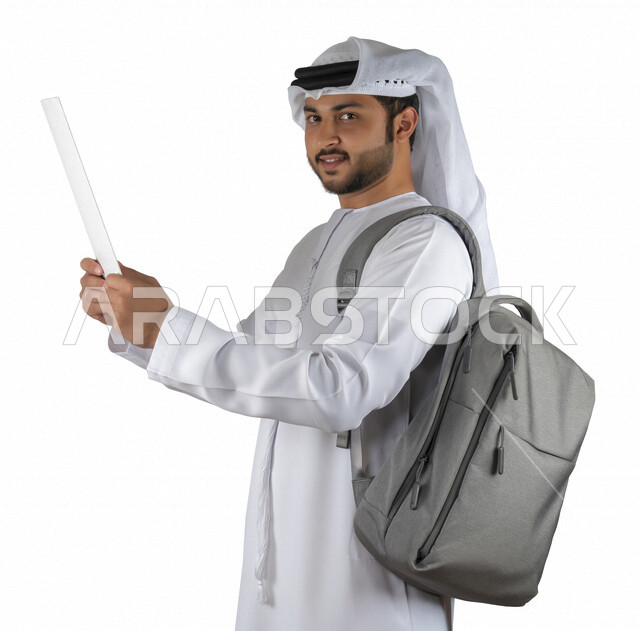 بورتريه طالب جامعي عربي خليجي اماراتي يضع الحقيبة على ظهرة ، يحمل بيده كتاب جامعي، قراءة الكتب الجامعية، مراجعة الدروس اليومية، التعليم الجامعي في الإمارات العربية المتحدة ، خلفية بيضاء .