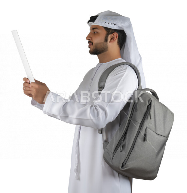 بورتريه طالب جامعي عربي خليجي اماراتي يضع الحقيبة على ظهرة ، يحمل بيده كتاب جامعي، قراءة الكتب الجامعية، مراجعة الدروس اليومية، التعليم الجامعي في الإمارات العربية المتحدة ، خلفية بيضاء .