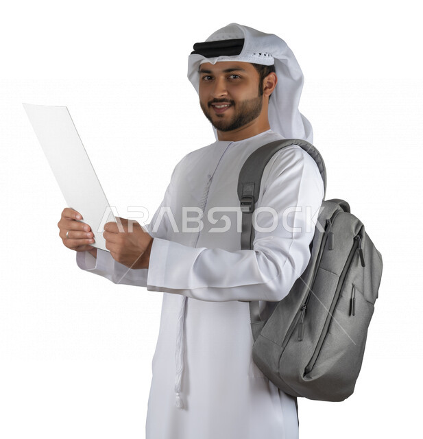 بورتريه طالب جامعي عربي خليجي اماراتي يضع الحقيبة على ظهرة ، يحمل بيده كتاب جامعي، قراءة الكتب الجامعية، مراجعة الدروس اليومية، التعليم الجامعي في الإمارات العربية المتحدة ، خلفية بيضاء .