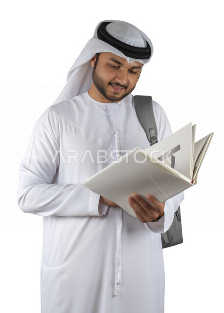 بورتريه طالب جامعي عربي خليجي اماراتي يضع الحقيبة على ظهرة ، يحمل بيده كتاب جامعي، قراءة الكتب الجامعية، مراجعة الدروس اليومية، التعليم الجامعي في الإمارات العربية المتحدة ، خلفية بيضاء .