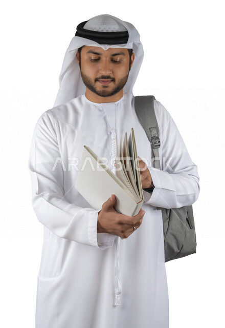 بورتريه طالب جامعي عربي خليجي اماراتي يضع الحقيبة على ظهرة ، يحمل بيده كتاب جامعي، قراءة الكتب الجامعية، مراجعة الدروس اليومية، التعليم الجامعي في الإمارات العربية المتحدة ، خلفية بيضاء .