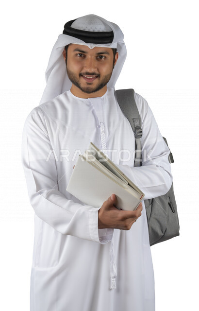 بورتريه طالب جامعي عربي خليجي اماراتي يضع الحقيبة على ظهرة ، يحمل بيده كتاب جامعي، قراءة الكتب الجامعية، مراجعة الدروس اليومية، التعليم الجامعي في الإمارات العربية المتحدة ، خلفية بيضاء .