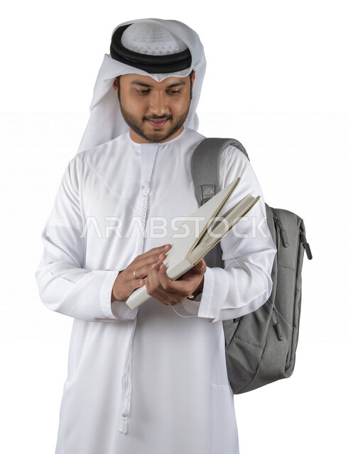 بورتريه طالب جامعي عربي خليجي اماراتي يضع الحقيبة على ظهرة ، يحمل بيده كتاب جامعي، قراءة الكتب الجامعية، مراجعة الدروس اليومية، التعليم الجامعي في الإمارات العربية المتحدة ، خلفية بيضاء .