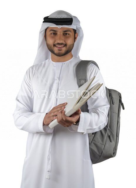بورتريه طالب جامعي عربي خليجي اماراتي يضع الحقيبة على ظهرة ، يحمل بيده كتاب جامعي، قراءة الكتب الجامعية، مراجعة الدروس اليومية، التعليم الجامعي في الإمارات العربية المتحدة ، خلفية بيضاء .
