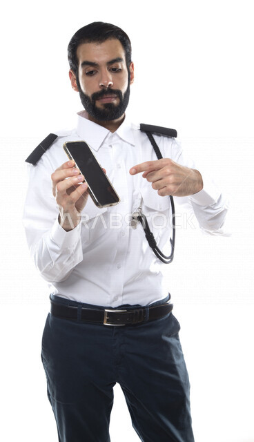 بورتريه رجل أمن عربي خليجي إماراتي يرتدي الزي الرسمي للعمل , يحمل بيده الهاتف المحمول , إشارات يد تؤشر للتقنية , مهن و وظائف , استخدام التقنية الحديثة للحفاظ على الأمن والسلامة , خلفية بيضاء .