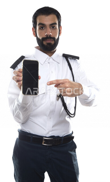 بورتريه رجل أمن عربي خليجي إماراتي يرتدي الزي الرسمي للعمل , يحمل بيده الهاتف المحمول , إشارات يد تؤشر للتقنية , مهن و وظائف , استخدام التقنية الحديثة للحفاظ على الأمن والسلامة , خلفية بيضاء .