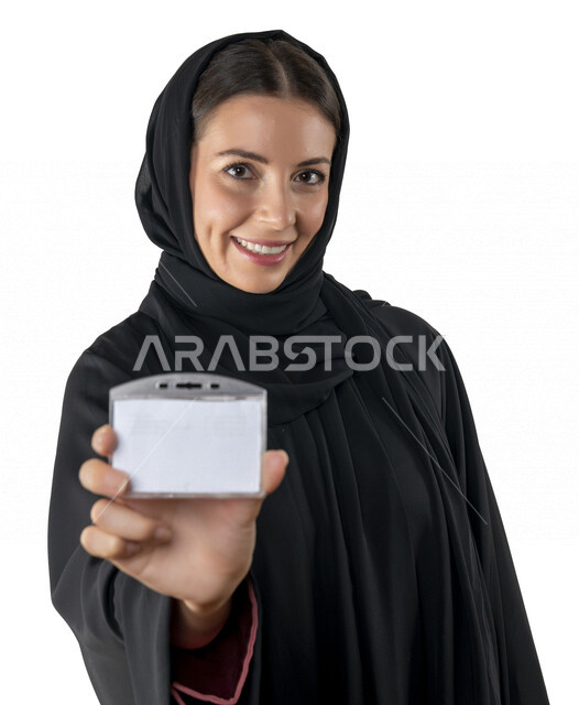 بورتريه لإمرأه عربيه إماراتيه خليجيه محجبه مبتسمه, تمسك بيدها بطاقة بيضاء فارغه، تنظر الى الكاميرا, بادج شخصي, طالبه جامعيه، موظفه, هوية شخصيه, بطاقة تعريفيه, خلفية بيضاء