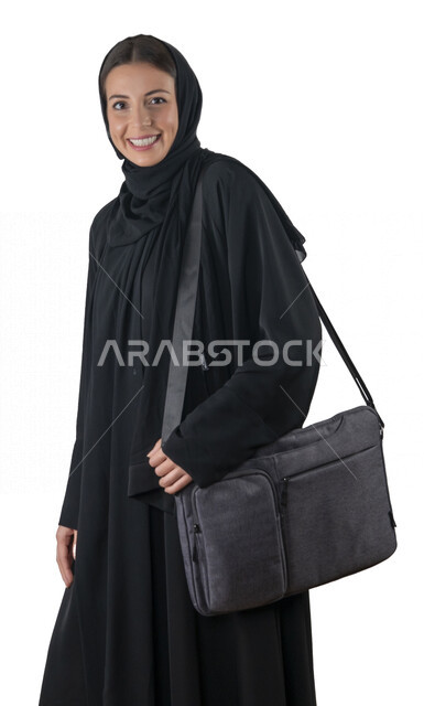 بورتريه لطالبة جامعية عربية إماراتيه خليجية محجبة مبتسمه تحمل حقيبة اللابتوب على كتفها, تنظر الى الكاميرا, موظفه في شركه إماراتيه, شابة متشوقة للذهاب الى العمل, خلفية بيضاء