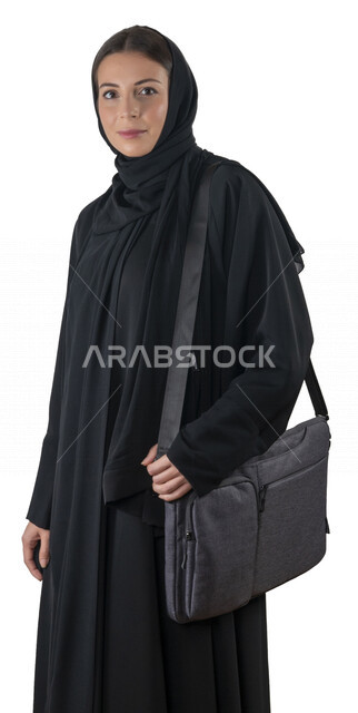 بورتريه لطالبة جامعية عربية إماراتيه خليجية محجبة مبتسمه تحمل حقيبة اللابتوب على كتفها, تنظر الى الكاميرا, موظفه في شركه إماراتيه, شابة متشوقة للذهاب الى العمل, خلفية بيضاء
