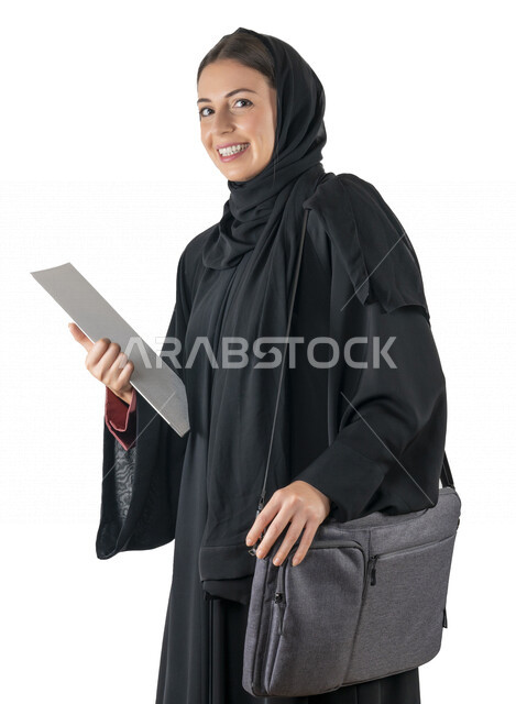 بورتريه لطالبة جامعية عربية إماراتيه خليجية محجبة مبتسمه تحمل حقيبة اللابتوب على كتفها, تمسك بيدها أوراق عمل, تنظر الى الكاميرا, موظفه في شركه إماراتيه, شابة متشوقة للذهاب الى العمل, خلفية بيضاء