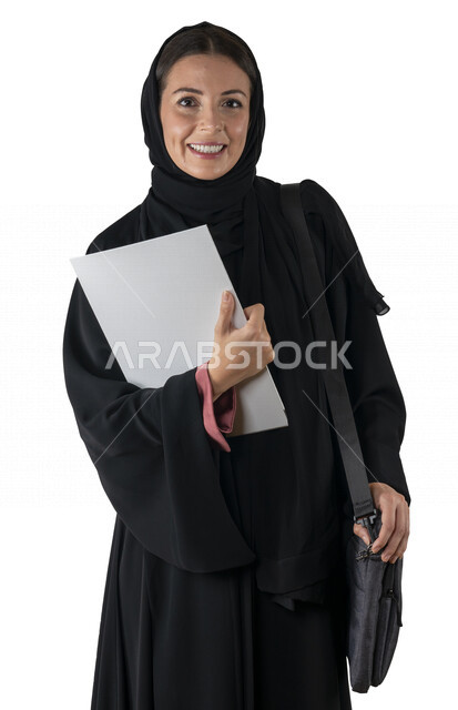 بورتريه لطالبة جامعية عربية إماراتيه خليجية محجبة مبتسمه تحمل حقيبة اللابتوب على كتفها, تمسك بيدها أوراق عمل, تنظر الى الكاميرا, موظفه في شركه إماراتيه, شابة متشوقة للذهاب الى العمل, خلفية بيضاء