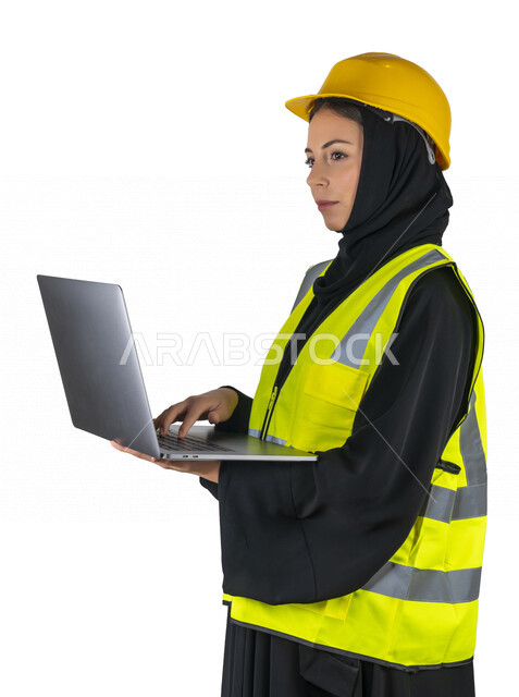بورتريه لمهندسة معمارية عربية إماراتيه خليجية تحمل بيدها جهاز اللابتوب المحمول ، مهندسة إنشاءات محجبة ترتدي بدلة السلامة في العمل، خوذة العمل، مهن ووظائف هندسيه، مشروع بناء، مفهوم الهندسه المعماريه, خلفية بيضاء