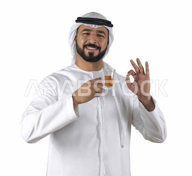 بورتريه لرجل عربي خليجي إماراتي مبتسم يرتدي الزي الإماراتي التقليدي , يحمل بيده كوب من الشاي الأحمر, إحتساء الشاي الساخن , الإستمتاع بالمشروبات الدافئة , أعشاب الشاي , قضاء وقت ممتع و هادئ , خلفية بيضاء, الضيافه السعوديه, مشروبات ساخنه