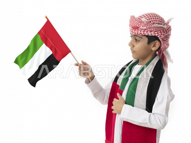 النظر إلى العلم, الإحتفال بيوم الاستقلال الوطني لدولة الإمارات العربية المتحدة, بورتريه مقرب لولد عربي خليجي اماراتي يرتدي العمامه والكندوره الاماراتيه يحمل بيده ويرتدي علم الإمارات, هوية اليوم الوطني الإماراتي51, تقديم الولاء والحب للوطن, خلفية بيضاء