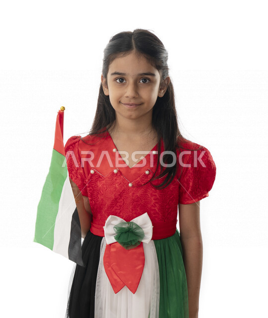الإحتفال بيوم الاستقلال لدولة الإمارات العربية المتحدة, بورتريه مقرب لبنت عربية خليجية إماراتية ترتدي فستان بألوان علم الإمارات, هوية اليوم الوطني الإماراتي51, فتاة تحمل بيدها علم الامارات وتنظر الى الكاميرا, تقديم الولاء والحب للوطن, خلفية بيضاء