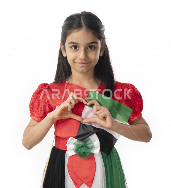 تقديم الولاء والحب للوطن, الإحتفال بيوم الاستقلال لدولة الإمارات العربية المتحدة, بورتريه مقرب لبنت عربية خليجية إماراتية ترتدي فستان بألوان علم الإمارات وتنظر إلى الكاميرا, هوية اليوم الوطني الإماراتي51, ايماءات يد على شكل قلب, خلفية بيضاء