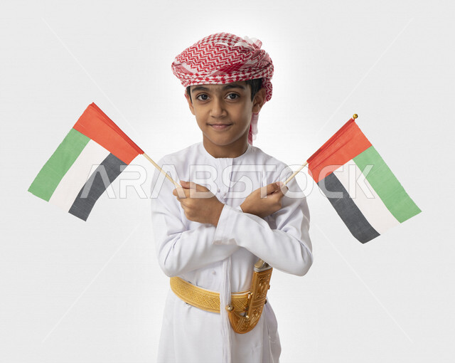 الإحتفال بيوم الاستقلال الوطني لدولة الإمارات العربية المتحدة, بورتريه مقرب لولد عربي خليجي اماراتي يرتدي الزي التقليدي الاماراتي يحمل بيديه أعلام الإمارات, إيماءات الفرح والسعادة, هوية اليوم الوطني الإماراتي51, تقديم الولاء والحب للوطن, خلفية بيضاء