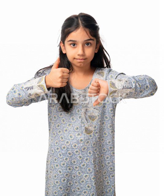 الحيرة والتردد في شيء ما، بورتريه مقرب لفتاة عربية اماراتية بإيماءات يد تدل على عدم الموافقه والموافقه, عدم الإعجاب والإعجاب, الرفض و القبول, بنت سعودي ترتدي الثوب الخليجي و ترفع أصبع الإبهام للأعلى و للأسفل, خفية بيضاء