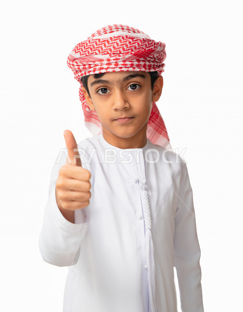 Face and hand gestures indicating approval, a portrait of an Arab-Emirati-Gulf boy wearing a turban and an Emirati kandora raising his thumb with the sign of quality, admiration, satisfaction, and happiness, white background