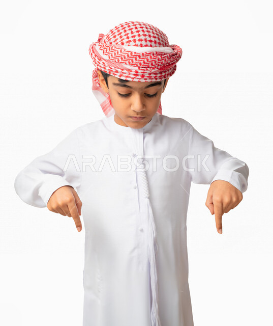 إيماءات يدين تشير الى موقع معين, بورتريه لولد عربي اماراتي خليجي يرتدي الكندورة والعمامة الاماراتية ويشير بأصابعه إلى الاسفل, حركات تدل على هذا المكان (هنا), في هذه اللحظه (الآن), خلفية بيضاء
