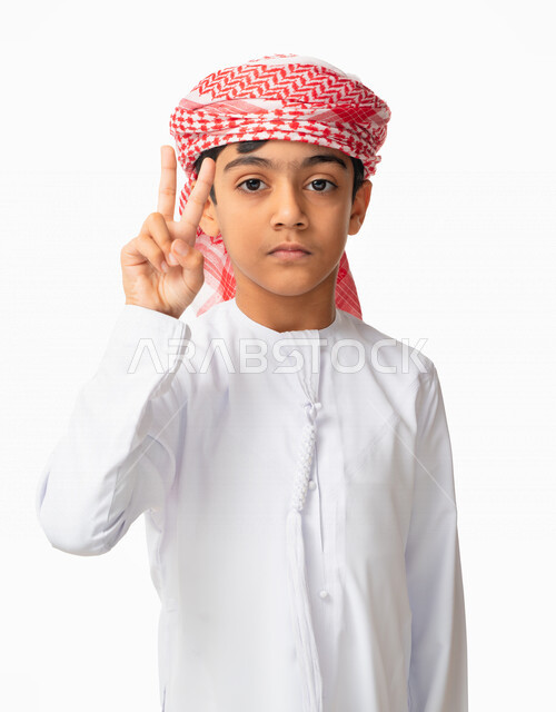 رفع الاصابع الى الأعلى بعلامة النصر و القوة, بورتريه لطفل عربي اماراتي خليجي يرتدي الكندورة والعمامة الاماراتية ،ايماءات وجه ويدين تدل على الفوز والإنتصار, تحقيق الاهداف و إنجاز المهامات , الإعجاب والرضا و الشعور بالسعاده، خلفية بيضاء