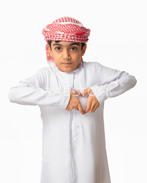 السعاده والطمأنينه و المحبه والهيام, بورتريه لطفل عربي اماراتي خليجي يرتدي الكندورة والعمامة الاماراتية , إيماءات يدين تدل على الشعور بالحب, الوقوع في الغرام, رفع اليدين بشكل قلب، عيد الحب (الفالنتاين)، خلفية بيضاء